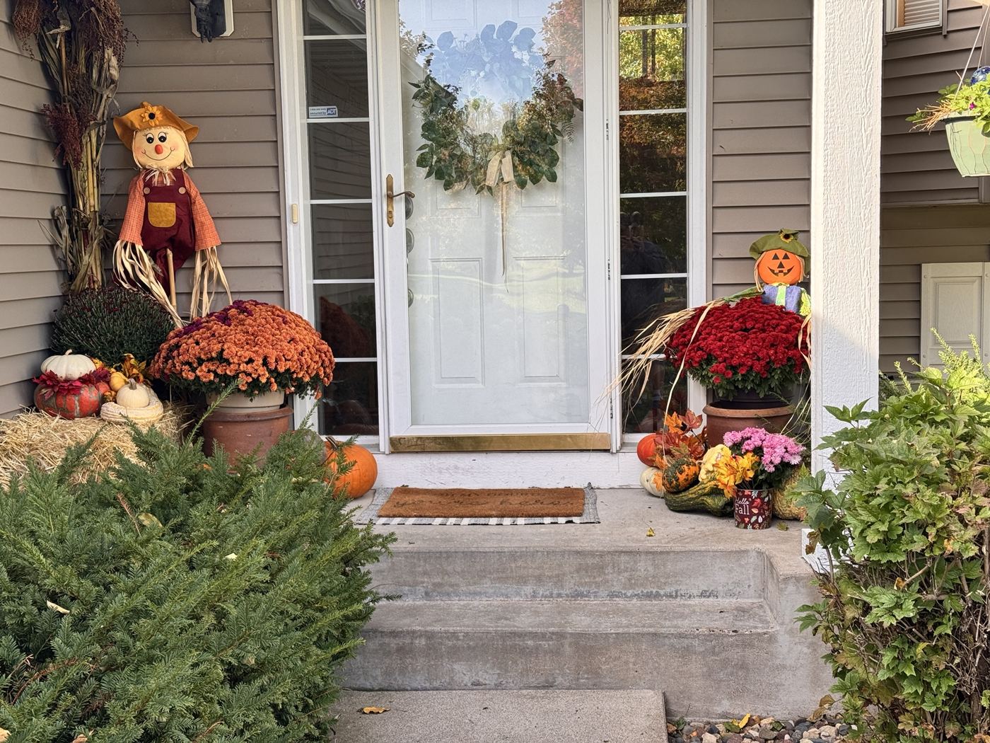 Front door with scarecrows, red and orange mums, gourds and a straw bale